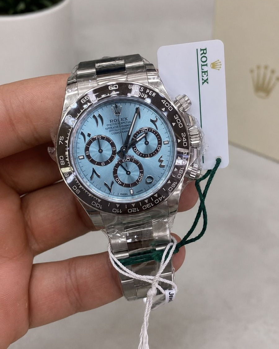 A Rolex Daytona watch with a light blue dial and stainless steel bracelet, held in a hand with its original tag attached.